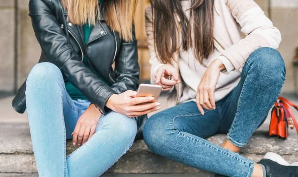Young friends watching on mobile phone while sitting on stairs outdoor - Millennial people having fun with new trends smartphone app - Generation z, technology and youth lifestyle