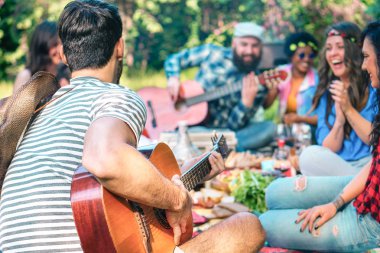 Young people doing picnic and playing guitar in park - Group of happy friends having fun during the weekend outdoor - Friendship, food and drink, funny activities and youth lifestyle concept clipart