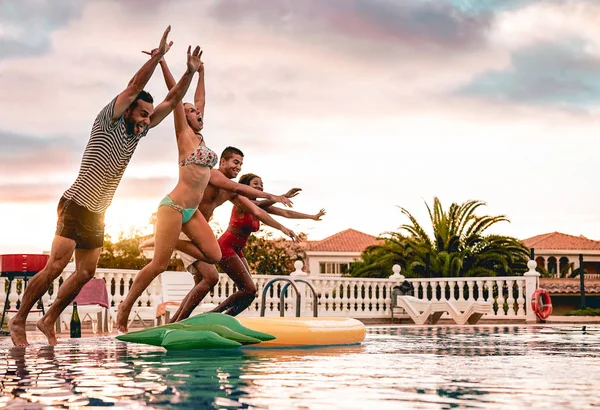 Group of happy friends jumping in pool at sunset time - Millennial young people having fun making party in exclusive resort tropical - Holidays, summer, vacation and youth lifestyle concept