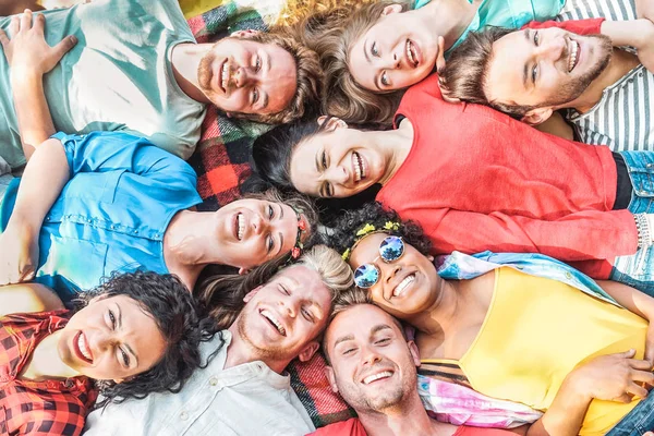 Grupo de amigos diversos que se divierten al aire libre - Jóvenes felices tumbados en la hierba después del picnic y riendo juntos - Amistad, unidad, concepto de estilo de vida milenario y juvenil —  Fotos de Stock