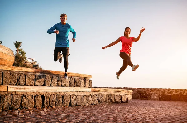 Pareja en forma haciendo sesión de entrenamiento al atardecer al aire libre - Jóvenes deportistas corriendo junto a la playa - Estilo de vida saludable y concepto deportivo —  Fotos de Stock