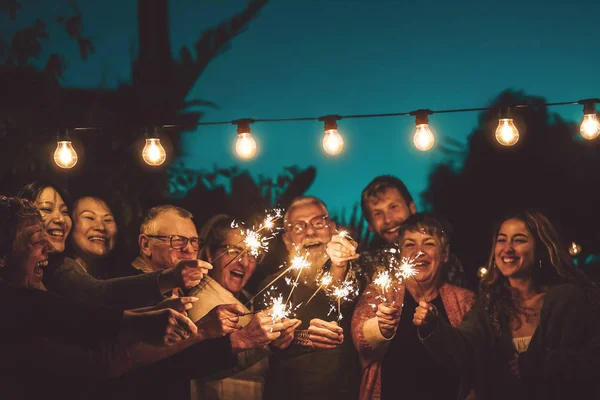 Glückliche Familie feiert mit Wunderkerze bei nächtlicher Party im Freien - Gruppe von Menschen unterschiedlichen Alters und ethnischer Zugehörigkeit vergnügt sich gemeinsam draußen - Freundschaft, Vorabend und Festkonzept — Stockfoto