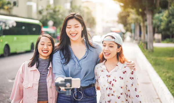 Amigos asiáticos felices vlogging en la estación de autobuses de la ciudad - Los jóvenes de moda utilizando el teléfono inteligente gimbal al aire libre - Amistad, tecnología, estilo de vida juvenil y concepto de redes sociales — Foto de Stock