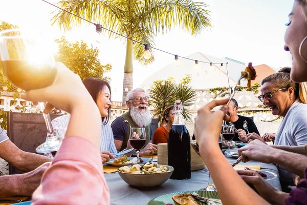 Šťastná rodina dělá večeři při západu slunce čas venkovní - skupina různorodých přátel baví spolu stolování venku - pojmu životní styl lidí, jídlo a víkendové aktivity — Stock fotografie