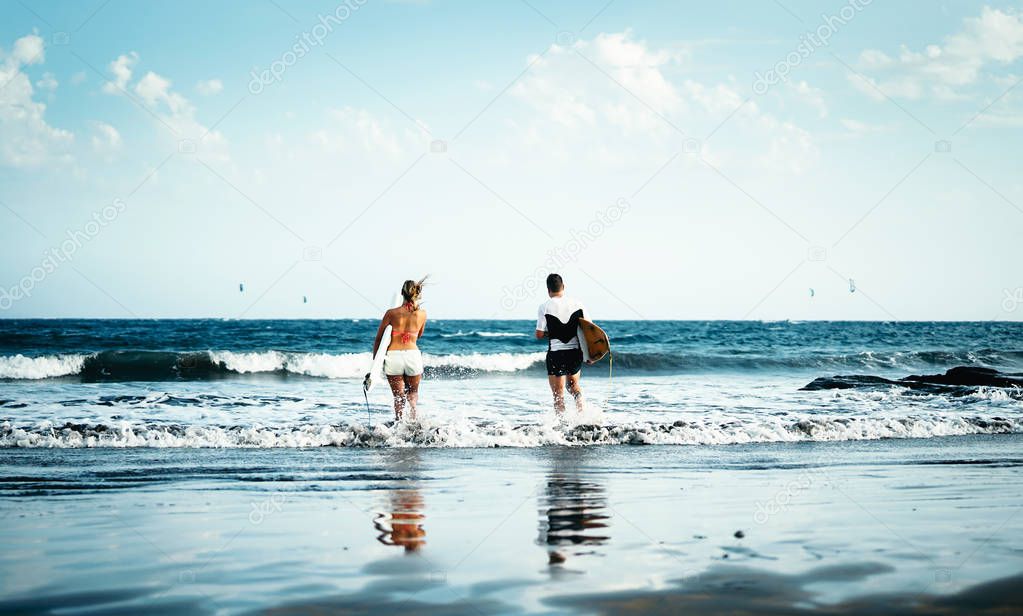Happy surfer couple going to surf - Sporty people having fun surfing in the ocean - Extreme sport and youth lifestyle concept