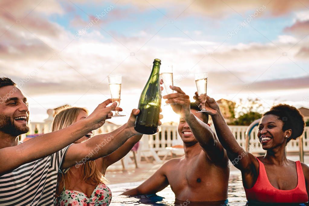 Happy friends doing pool party toasting champagne at sunset - Young people having fun drinking sparkling wine in luxury tropical beach resort - Holidays, vacation, summer and youth lifestyle concept