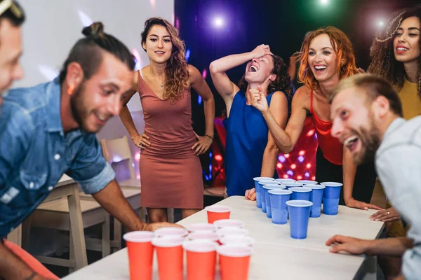 Happy friends playing beer pong in a cocktail bar - Jovens millennial people having fun doing party alcohol games at night pub - Conceito de vida noturna de amizade e juventude — Fotografia de Stock