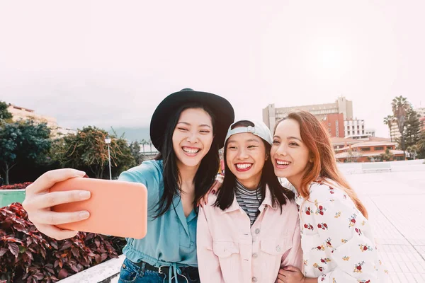 Chicas asiáticas felices tomando selfie con teléfono inteligente móvil al aire libre - Joven adolescente de moda divirtiéndose con la aplicación de nueva tecnología - Gente, social, medios de comunicación, amistad, tecnología y estilo de vida juvenil concepto de la gente — Foto de Stock