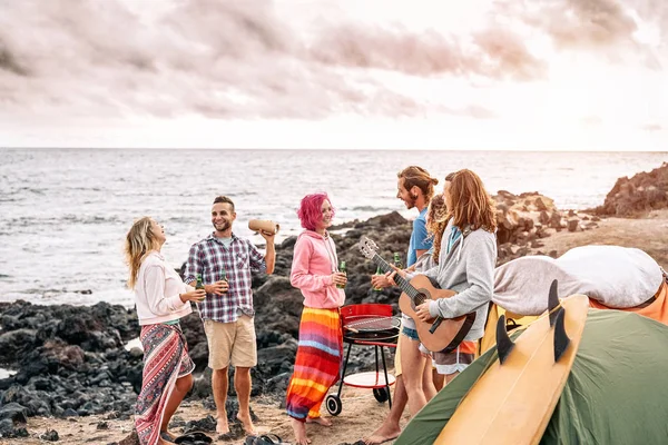 Χαρούμενοι σέρφερ φίλοι κάνουν πάρτι στο ηλιοβασίλεμα, ενώ camping δίπλα στην παραλία-νέοι άνθρωποι διασκεδάζουν και πίνοντας μπύρα υπαίθρια-Χιλιαία, καλοκαίρι, διακοπές και νεανικές διακοπές ζωής concept — Φωτογραφία Αρχείου