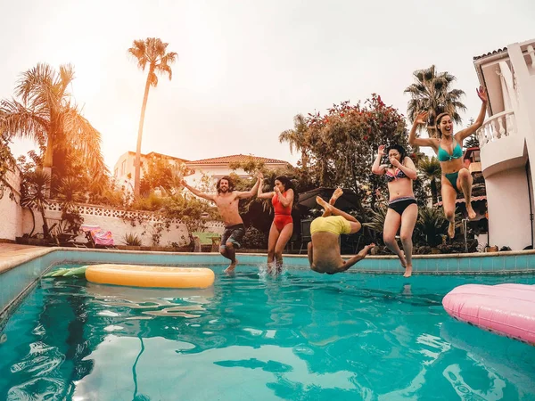 Grupo de amigos felices saltando en la piscina al atardecer - Jóvenes locos divirtiéndose haciendo fiesta en casa tropical exclusiva - Vacaciones, verano, vacaciones y concepto de estilo de vida juvenil — Foto de Stock