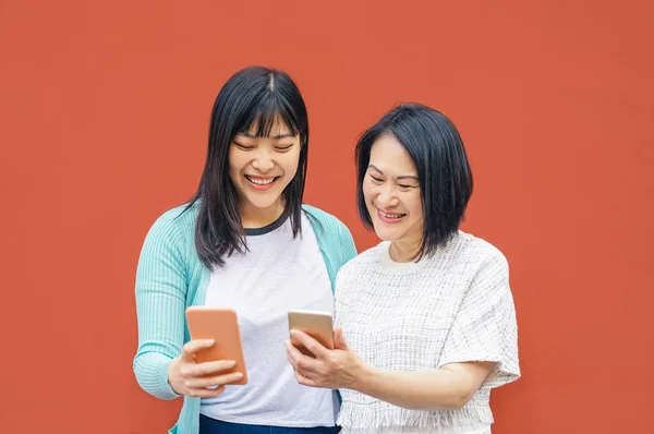 Madre e hija asiáticas usando teléfonos inteligentes móviles al aire libre - Familia china feliz divirtiéndose con nuevas tendencias aplicaciones tecnológicas para redes sociales - Concepto de personas sociales, tecnológicas y de estilo de vida —  Fotos de Stock