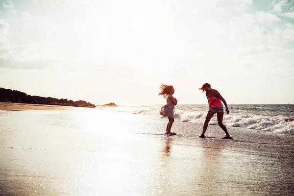 Madre e figlia felici che si divertono sulla spiaggia tropicale al tramonto - Famiglia che gioca il prossimo mare durante le vacanze estive - Concetto di genitore, amore e felicità — Foto Stock