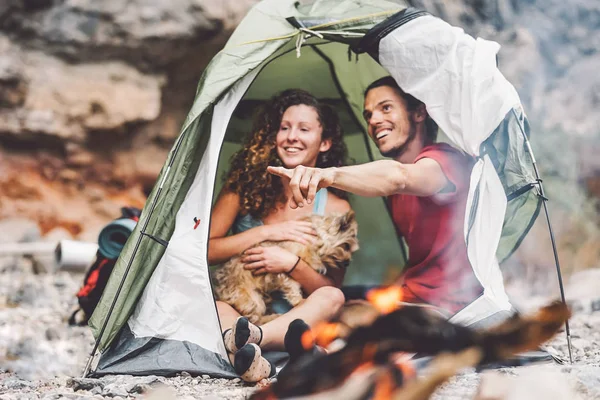 Beberapa trekker duduk di tenda dengan hewan peliharaan mereka - Happy man dan wanita bersenang-senang dalam liburan berkemah di sekitar gunung batu di samping api - Cinta, perjalanan dan konsep hubungan — Stok Foto