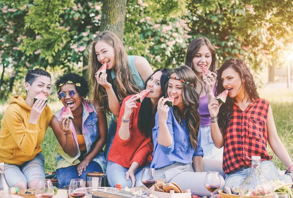 Chicas felices comiendo sandía en la cena de picnic en el jardín - Mujeres jóvenes divirtiéndose disfrutando del almuerzo juntas en el patio trasero - Amistad, comida, actividades de fin de semana y concepto de estilo de vida juvenil —  Fotos de Stock