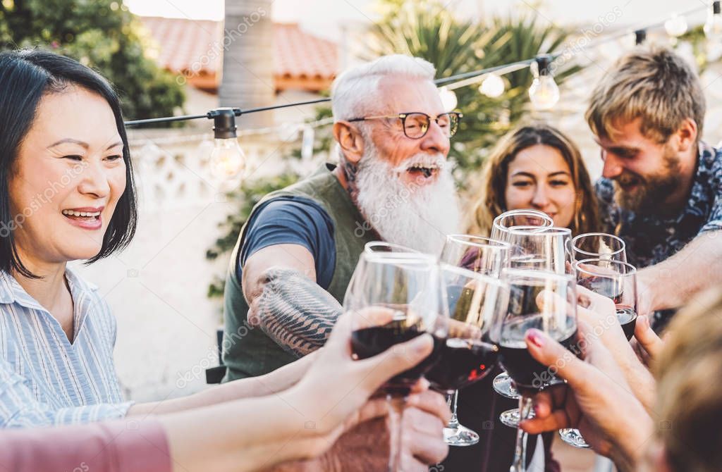 Happy family cheering and toasting with red wine glasses at dinner outdoor - People with different ages and ethnicity having fun at bbq party - food and drink, retired and young people concept