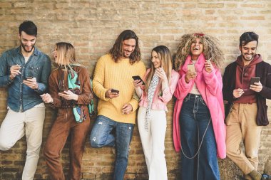 Dışarıda cep telefonu kullanan arkadaş grubu - Şehir merkezinde sigara içerken akıllı telefon uygulamalarıyla eğlenen genç mutlu insanlar - Bağımlılık, teknoloji ve gençlik yaşam tarzı konsepti