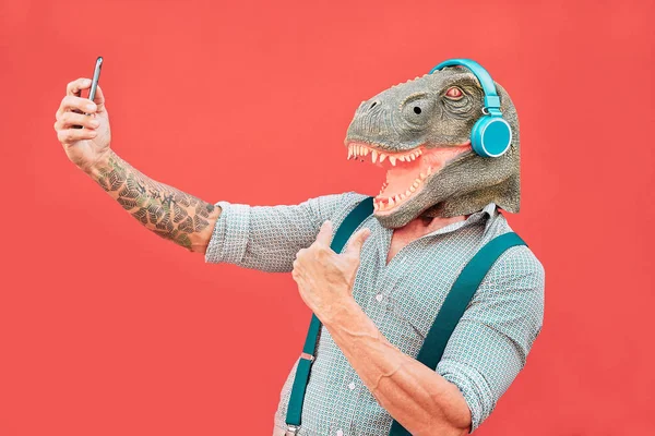 Homme âgé fou portant un masque t-rex et prenant selfie avec smartphone mobile - Hipster homme plus âgé s'amuser à écouter de la musique et danser en plein air - concepts absurdes, drôles et surréalistes — Photo