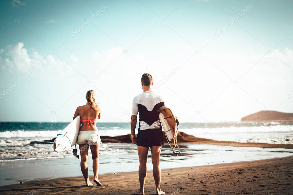 Couple of surfers standing on the beach with surfboards preparing to surf on high waves - Sporty young people having fun during a surfing day - Extreme sports, relationship and youth lifestyle concept