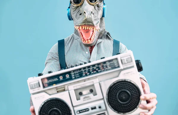 Loco hombre mayor con máscara t-rex y escuchar música celebración de vintage boombox estéreo al aire libre - Mascarada de moda masculina divertirse bailando y celebrando al aire libre - Concepto de gente absurda y divertida — Foto de Stock