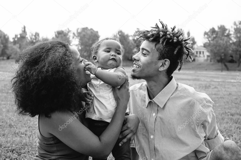 Happy African family enjoying a tender moment during the weekend outdoor - Mother and father having fun with their daughter in a public park - Love, parents and happiness concept