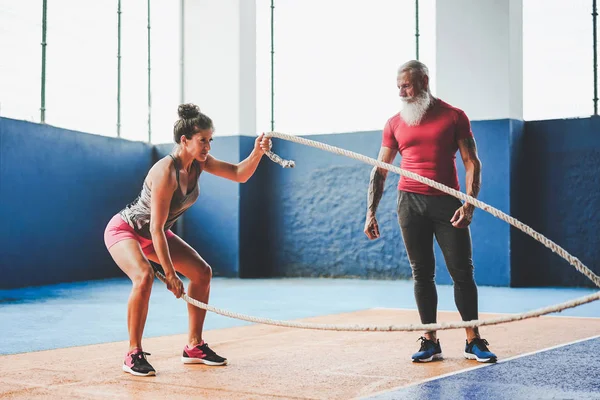 Adatta all'allenamento femminile con corda da battaglia all'interno della palestra - Personal trainer che motiva un'atleta donna a fare esercizi di sessione di allenamento - Wellness, concetto di stile di vita sportivo — Foto Stock