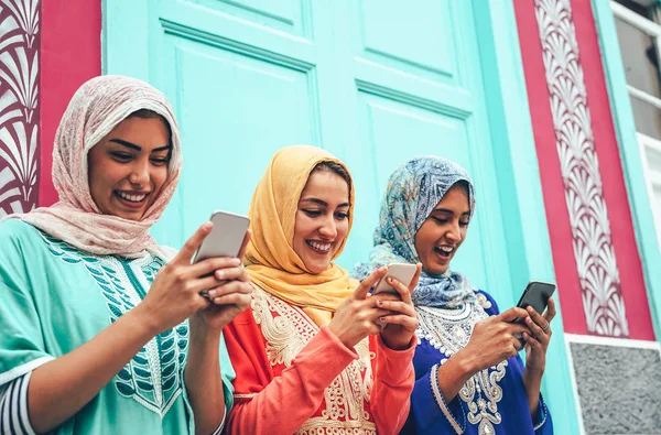 Joven amigo musulmán usando teléfonos inteligentes móviles en la universidad - Chicas árabes felices adictas a la nueva aplicación de tecnología de teléfono celular para las redes sociales - Millennial, religión, generación z y el concepto de tecnología —  Fotos de Stock