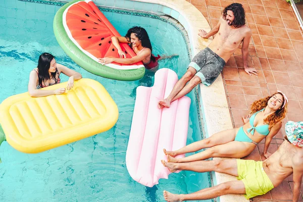 Happy friends having fun in swimming pool during summer tropical vacation - Young people relaxing and floating on air lilos in the pool resort - Friendship, relax, holidays and youth lifestyle concept — Stock Photo, Image