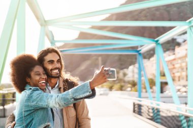 Happy smiling couple taking selfie with mobile smartphone outdoor - Young trendy people having fun during vacations - Social people technology addicted and travel trend lifestyle concept clipart