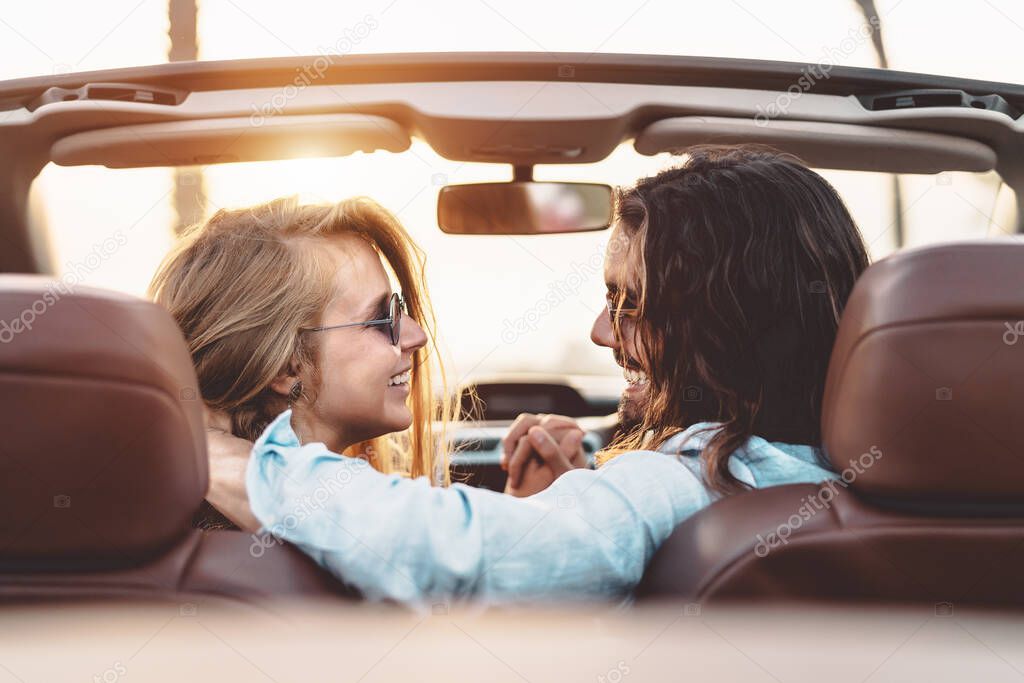 Happy young couple doing road trip in tropical city - Travel people having tender moments in trendy convertible car while discovering new places - Relationship and youth vacation lifestyle concept