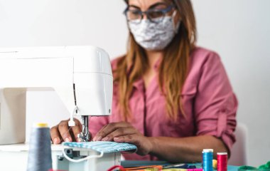 Dikiş makinesiyle çalışan olgun bir kadın Corona virüsünün yayılmasını önlemek ve önlemek için ev yapımı tıbbi maske takıyor.