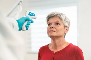 Corona virüsü salgını sırasında yaşlı kadın hastaya yeni dijital termometreyle sıcaklık ölçümü yapan doktor - Sağlık ve tıbbi ekipman konsepti