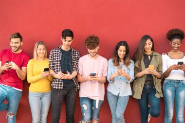 Genç arkadaşlar cep telefonlarını açık havada kullanıyor - Milenyum nesli yeni eğilimlerle eğleniyor sosyal medya uygulamaları - gençlik teknolojisi bağımlıları - kırmızı arka plan
