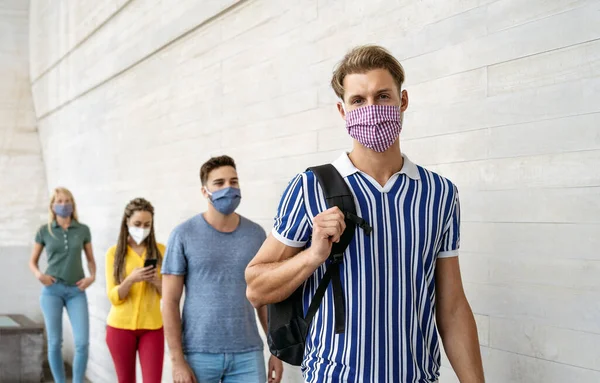 Young people from different cultures and race waiting in queue outside shop market while keeping social distance - Corona virus spread prevention concept