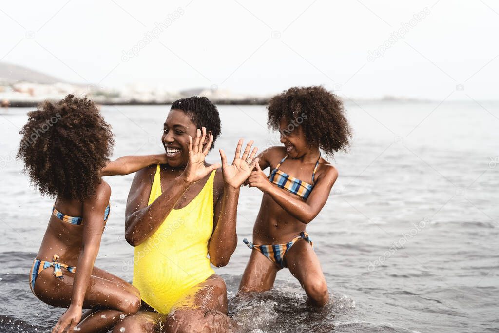 Happy African family playing on the beach during summer holidays - Afro American people having fun on vacation time - Parents love and travel lifestyle concept