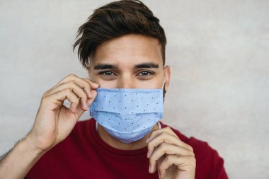 Young man wearing face mask portrait - Latin boy using protective facemask for preventing spread of corona virus - Health care and youth millennial people concept clipart