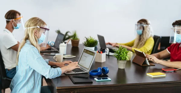 Young people in co-working creative space wearing surgical mask protection for preventing corona virus spread - Millennial friends working with ppe equipment - Social distancing and technology concept