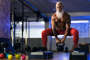 Kıdemli fitness görevlisi spor salonunda çaydanlık çanı egzersizi yapıyor - sağlıklı yaşam tarzı konsepti ve vücut geliştirme merkezindeki olgun erkek eğitimine uygun