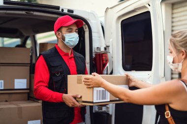 Coronavirus salgını sırasında Corona virüsünün yayılmasını önlemek için yüz koruma maskesi takan teslimatçı - Coronavirus salgını sırasında kostümcüye teslimat yapan genç ekspres kurye - teslimat ve online satın alma kavramı