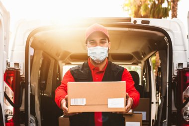 Corona virüsünün yayılmasını önlemek için yüz koruyucu maske takan teslimatçı Coronavirus salgını sırasında çalışan genç ekspres kurye teslimat ve çevrimiçi satın alma kavramı
