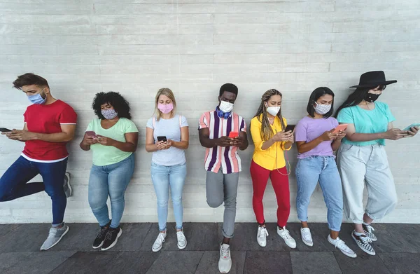 携帯電話の屋外でフェイスマスクを着用する若者 コロナウイルス発生中に新しい技術のソーシャルメディアアプリで楽しんでいる多人種の友人 若者の千年のライフスタイルの概念 — ストック写真