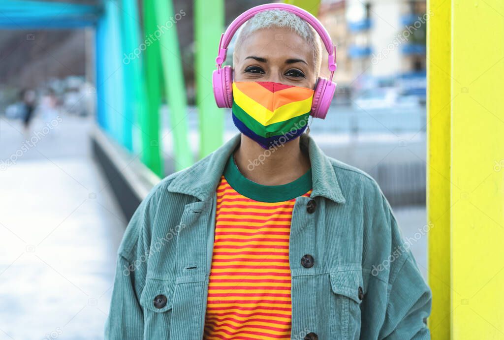 Young woman wearing gay pride mask while listening to music with headphones outdoor - Gender equality and technology concept