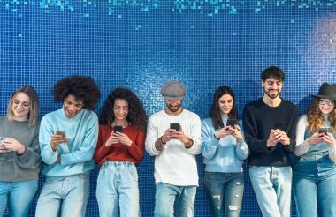 Gençler mavi arka planda dururken cep telefonu kullanıyor - Gençlik çağında yeni teknoloji sosyal medya uygulama kavramı bağımlısı