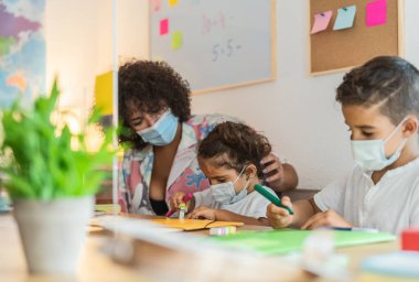 Corona virüsü salgını sırasında anaokulunda çocuk maskesi takan öğretmen - Sağlık ve Eğitim Konsepti