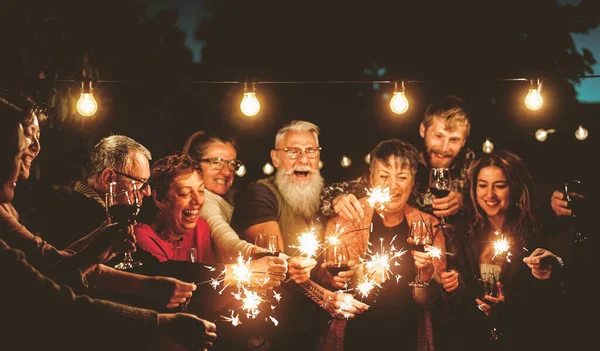 夜のパーティーで輝く花火で幸せな家族を祝う 一緒に楽しむ年齢や民族が異なる人々のグループ 休日のライフスタイルコンセプト — ストック写真
