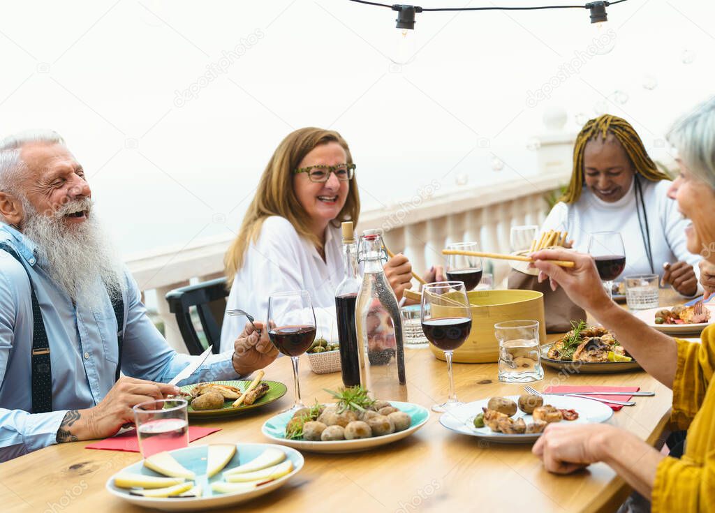 Multiracial seniors dining together at home terrace - Elderly people having fun at dinner on house patio - Food and drink concept
