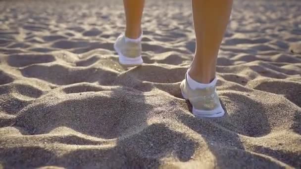 ženské nohy jsou spuštěn v trendy tenisky jsou posílení nad pískem ve slunečný den, výhled z zad