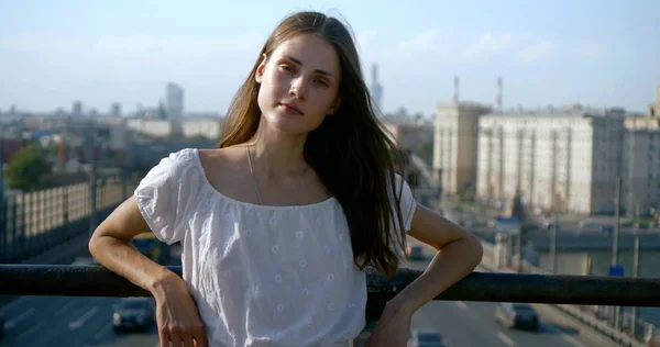 charming female city dweller is looking at camera outdoors on background of urban landscape