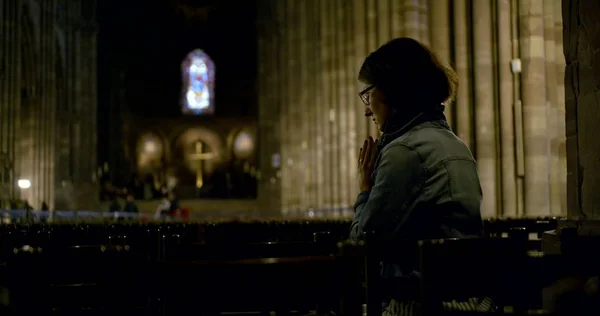 lady prays against blurry illuminated cross in darkness