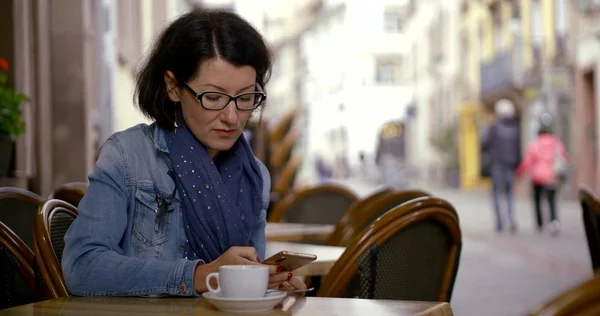 brunette types on modern smartphone sitting at cafe table