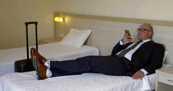 businessman talks on modern smartphone lying on bed